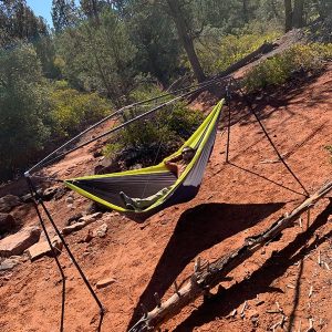 person lying in grey and green hammock on black hammock stand off the ground