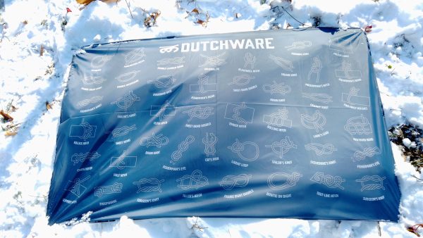 navy poly fabric cloth with symbols of knots and the word Dutchware printed on it laying flat on snowy grass in sunlight