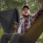 A hammock specialist relaxes in a Dutchware Half-Wit hammock, gazing at the sky as he contemplates which hammock quilts to purchase.