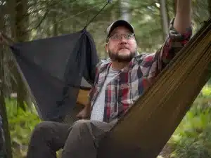 A hammock specialist relaxes in a Dutchware Half-Wit hammock, gazing at the sky as he contemplates which hammock quilts to purchase.